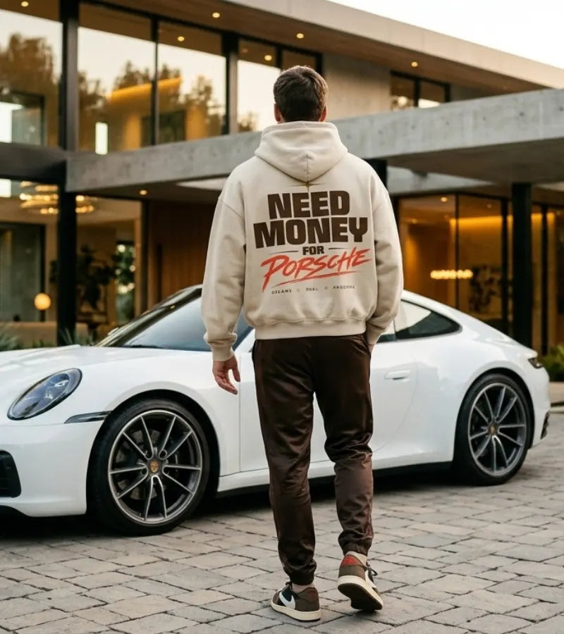 Model wearing a cream Porsche graphic hoodie from behind with large brown NEED MONEY lettering and coral-orange handwritten Porsche print