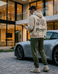 Model wearing a cream Porsche graphic hoodie from behind with green handwritten lettering, dark star and faint car silhouette on the back