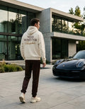 Model wearing a cream Need Money for Porsche hoodie with burgundy NEED MONEY FOR lettering and flowing gold Porsche script on the back