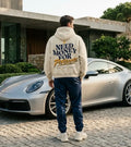Model wearing a cream Porsche graphic hoodie from behind with curved navy NEED MONEY FOR typography and golden Porsche brush lettering