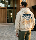 Model wearing a cream Porsche graphic hoodie from behind with curved charcoal NEED MONEY lettering, red Porsche script and Dreams Fuel Progress print
