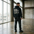 Model wearing black Porsche graphic hoodie with green and white speed stripes, bold typography and Higher Goals Bigger Miles detail