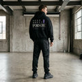 Model wearing a black Need Money for Porsche hoodie with bold ivory lettering, lavender star and vertical accent tab on the back