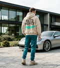 Model wearing a cream Porsche graphic hoodie from behind with distressed NEED MONEY lettering and bright mint-green handwritten Porsche print