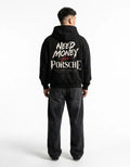 Model wearing a black Porsche racing graphic hoodie with red checkered flag, bold cream typography and Cars Dreams No Limits slogan