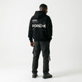 Model wearing a black Porsche graphic hoodie with modern white lettering, mint green line details and a four-point star back print